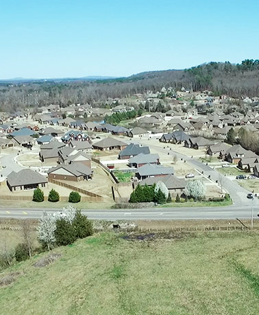 A different drone view of a neighborhood development surrounded by fields and trees in Priceville, AL.