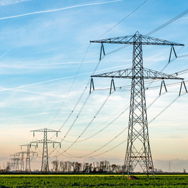 A view of electricity transmission towers disappearing into the distance underneath a blue and orange, cloud-streaked sky.